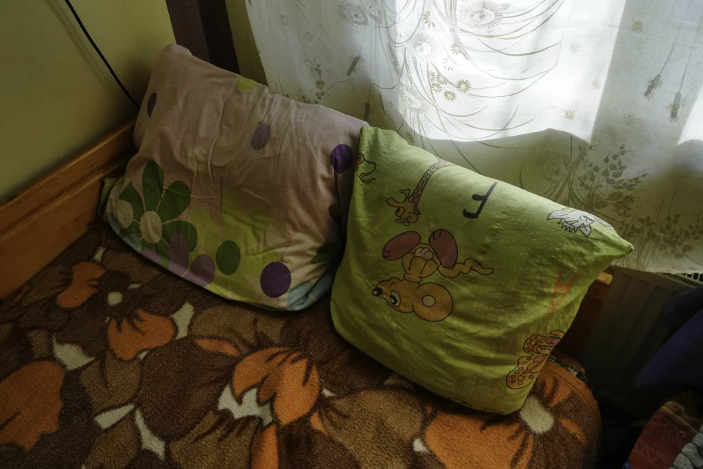 Two patterned pillows on a floral bedspread beside a curtained window