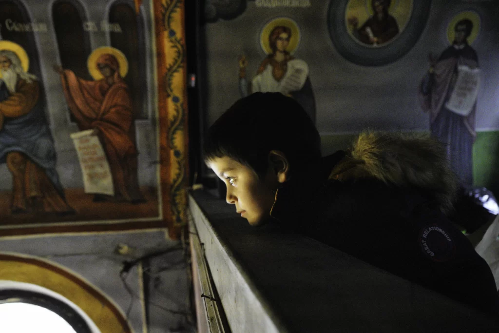 Boy leaning on a wooden ledge before Orthodox wall murals