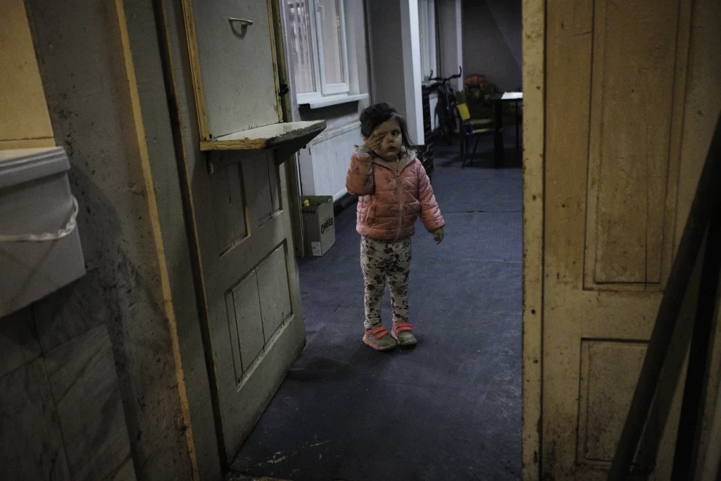Girl covering one eye, framed by wooden doors in a dim room