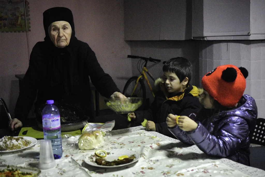 Woman in black serving food to seated children at a dimly lit table