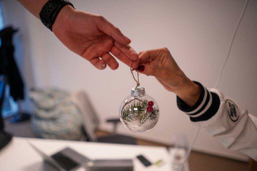 Hands exchanging a pine and berry ornament