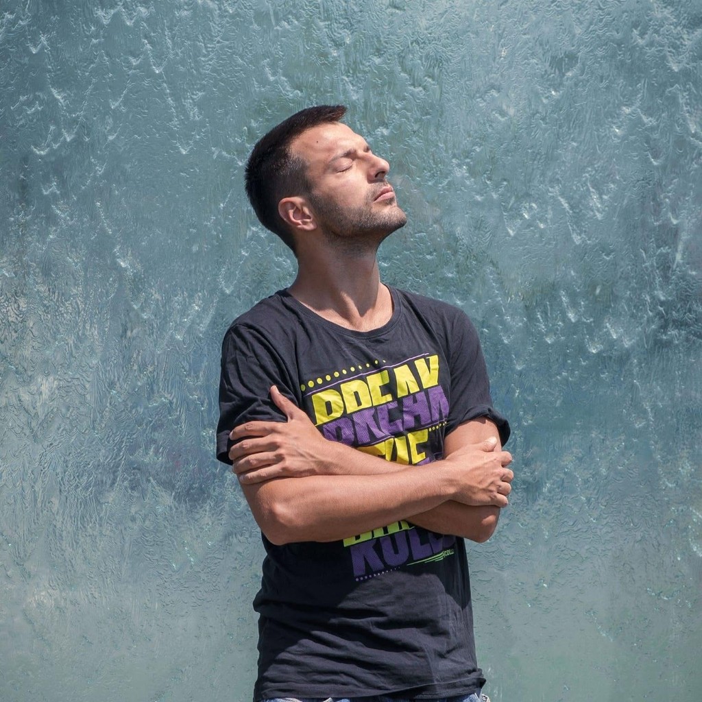 Portrait of Todor Stoyanov with eyes closed and arms crossed in front of a cascading water wall